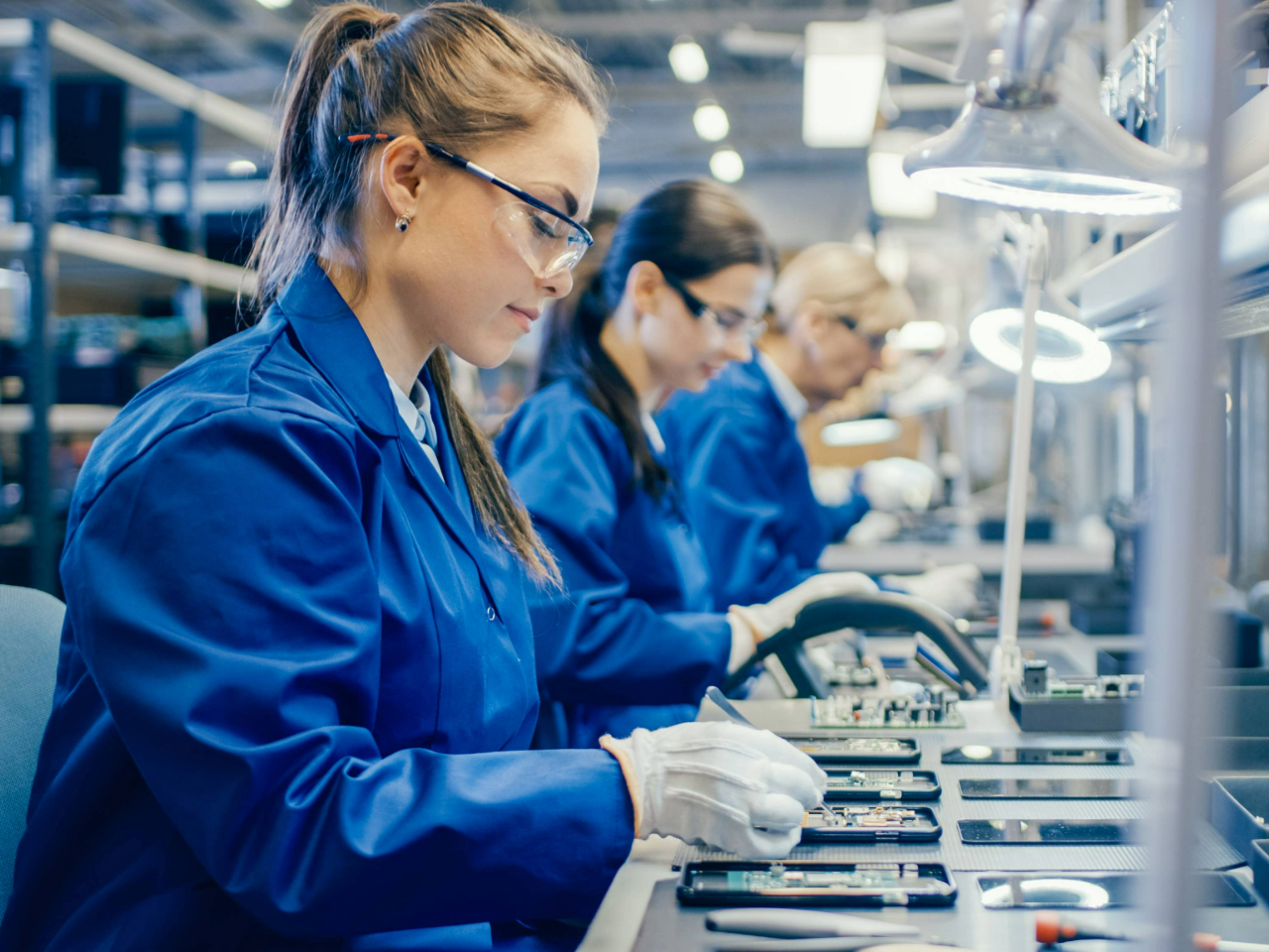 Women in blue uniforms work at an assembly line
