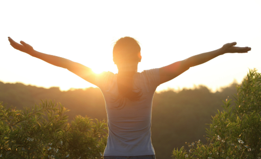 Women with her arms spread wide facing the sunrise 