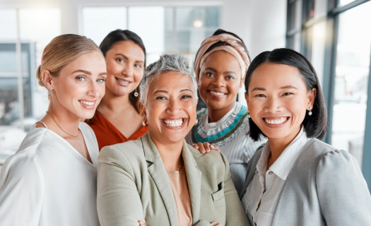 Five women in business attire smiling at the camera.