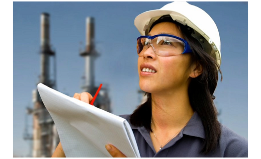 Woman with construction hat, safety glasses and notepad looking into the distance with industrial background