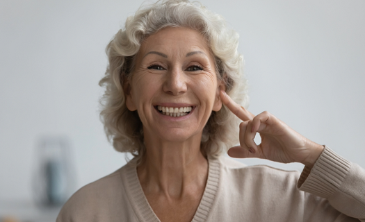 Senior woman pointing at her ear while smiling.
