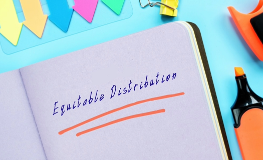 The words EQUITABLE DISTRIBUTION written on a notebook in pen with brightly colored office supplies all around it.