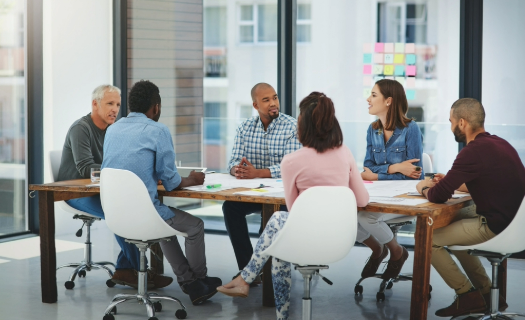 A group of people sit in a modern conference room having a conversation around a table.