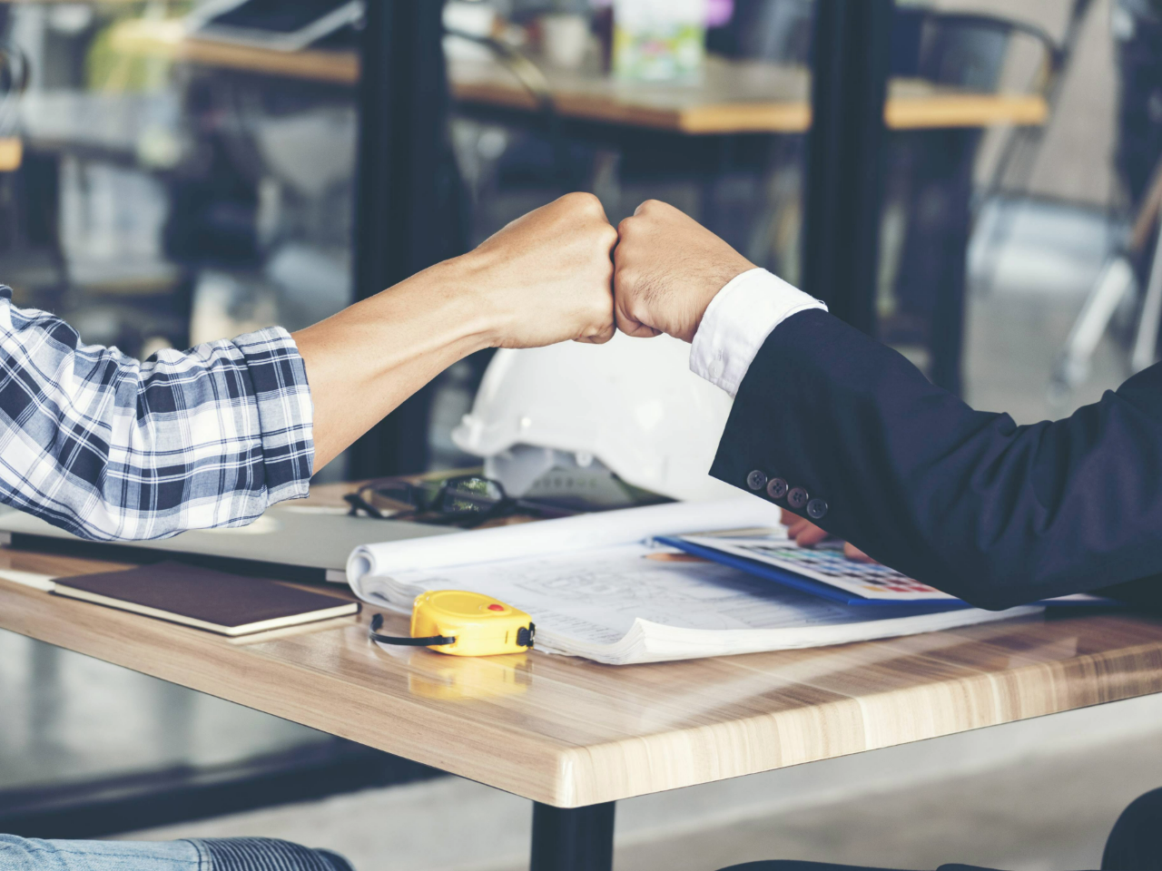 Two hands fist bumping over a table with documents and equipment on it