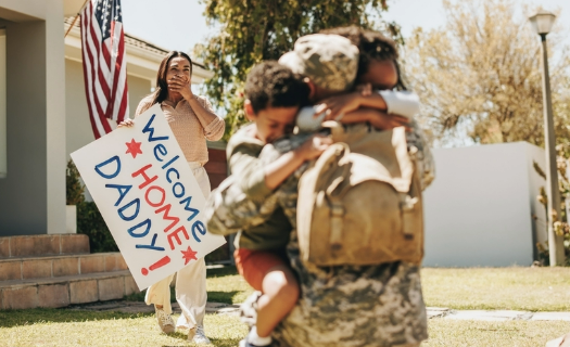 Soldier coming home to his wife and child in the front yard of a home.