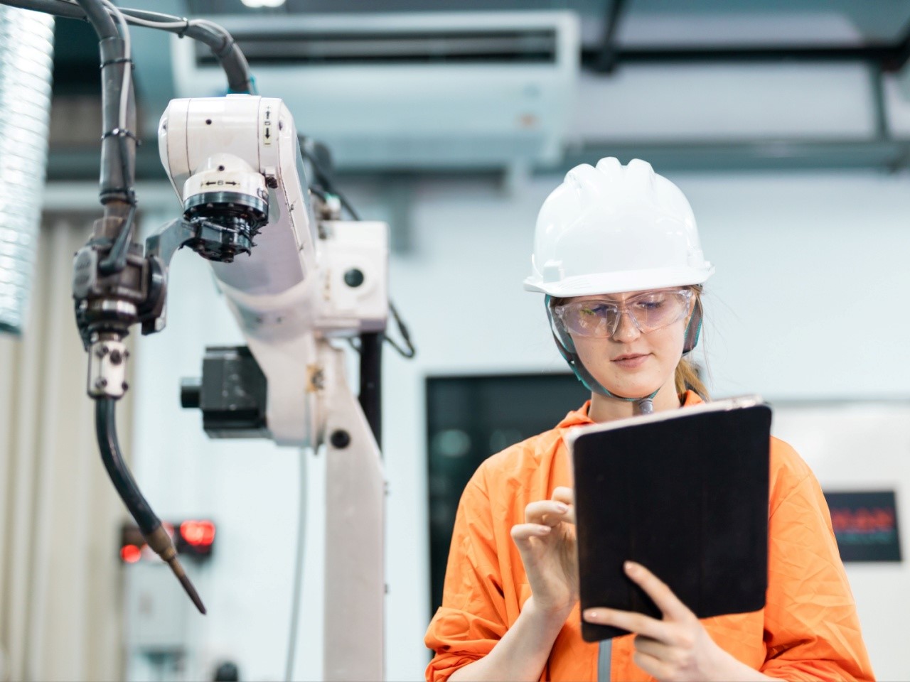 Female engineer using tablet to control robotic arm